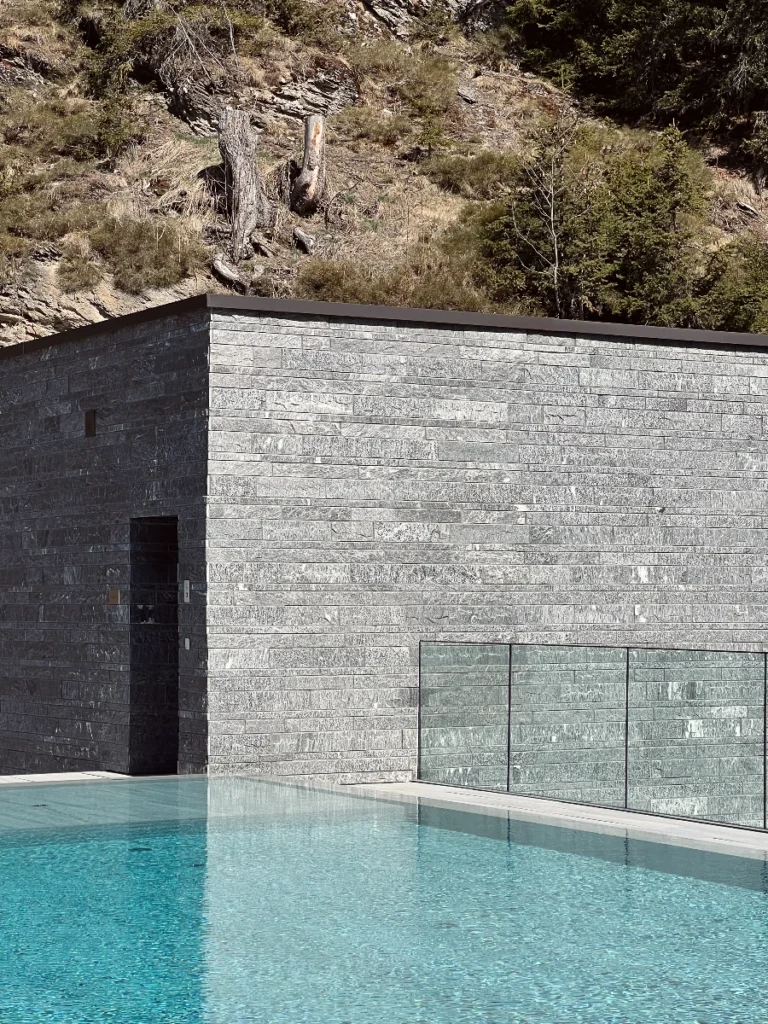 Between two chalet-like structures, on a stone podium, guests find the main outdoor swimming pool